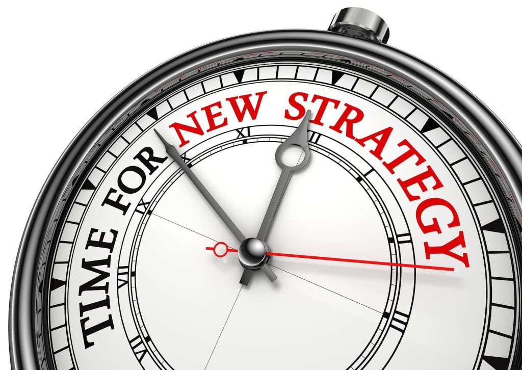 A close-up of a clock showing the words "TIME FOR NEW STRATEGY" in bold red letters, replacing traditional numbers. The clock hands point to unspecified positions, much like finding that perfect moment to start blogging about exciting new topics.
